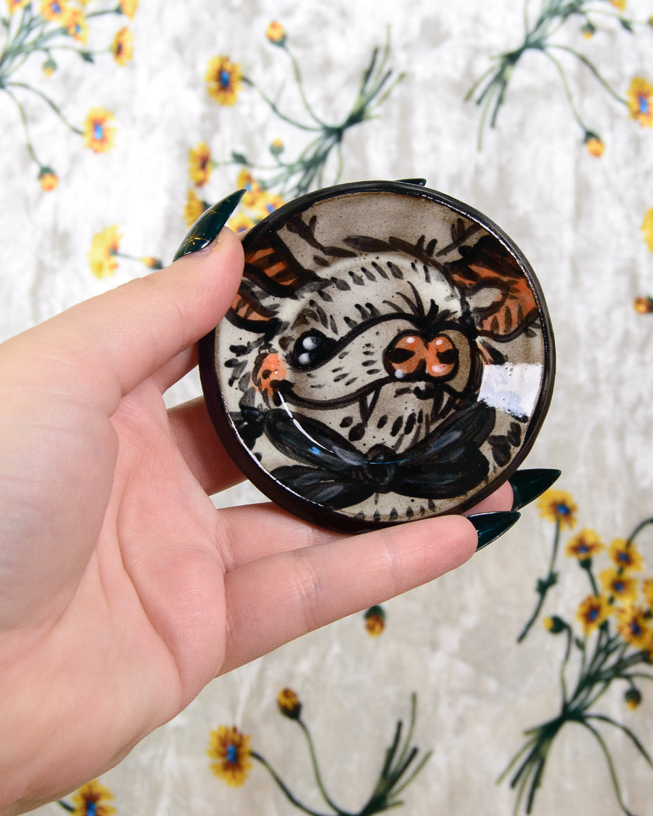 Hand holding a round ceramic coaster with a bat design against a floral background
