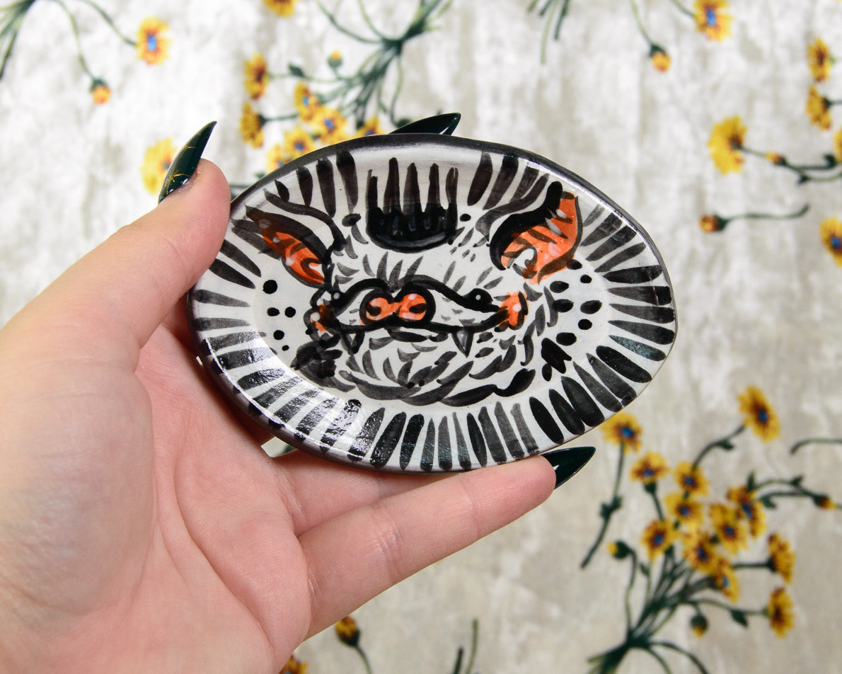 Hand holding a small ceramic dish with a cartoon bat design against a floral background