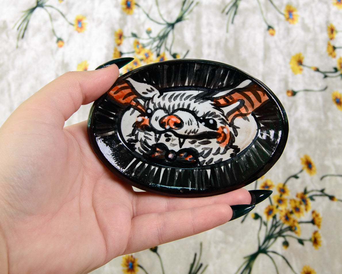 Hand holding a black dish with a painted bat design against a floral background