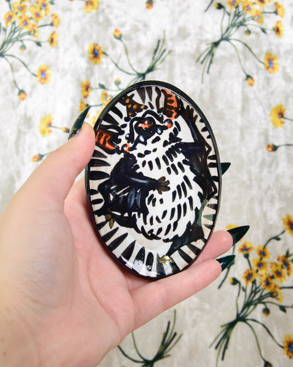 Hand holding a round ceramic dish with a black and white bat design against a floral background