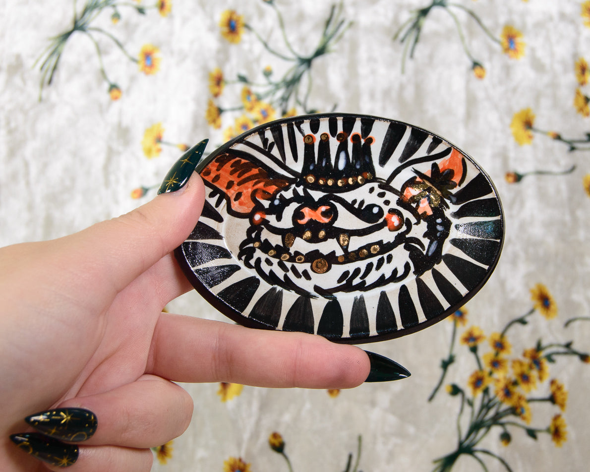 Hand holding a decorative circular ring dish with a bat design against a floral background