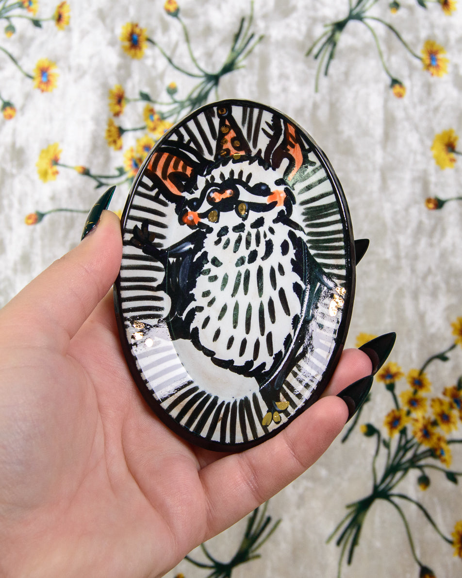 Hand holding a round, black and white decorative ring dish with a bat design against a floral background.