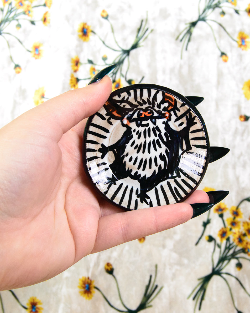 Hand holding a round black and white dish with a bat design against a floral background