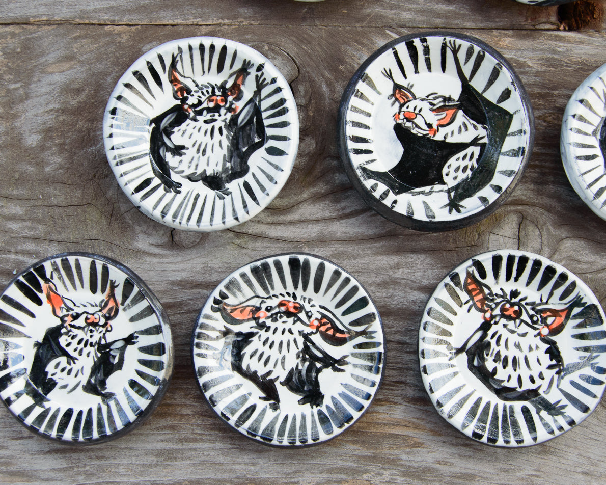 Set of five ceramic plates with bat designs on a wooden surface