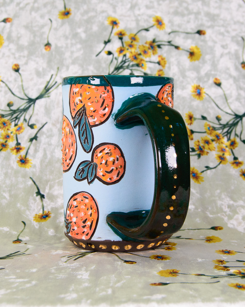 Ceramic mug with colorful fruit designs and a teal handle with gold dot details