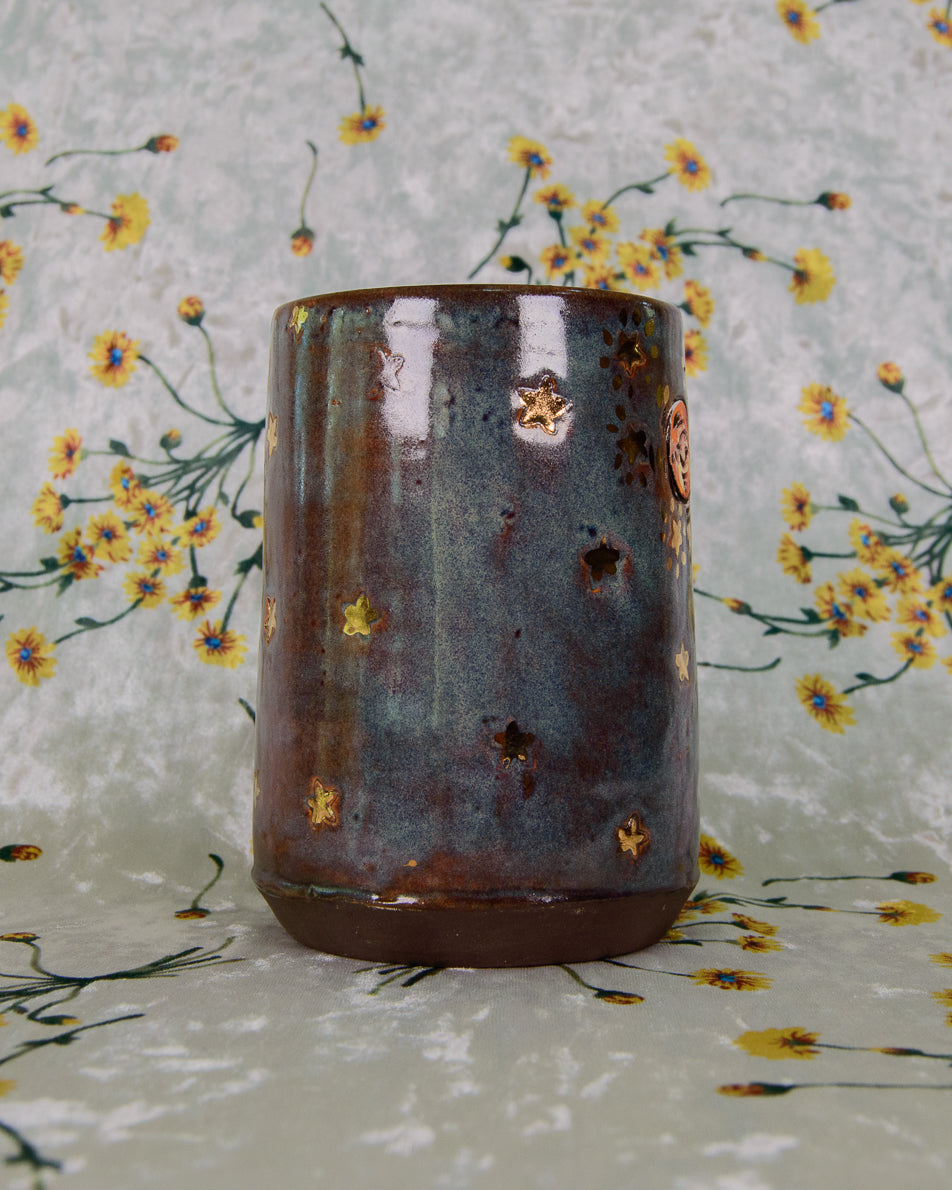 Ceramic cup with brown and blue glaze and gold stars on a floral-patterned background