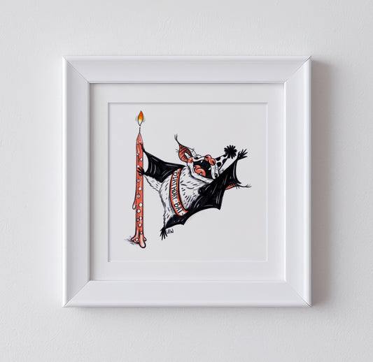 Framed artwork of a whimsical bat dancing around a birthday candle, wearing a sash that says "birthday bat". On a white background.