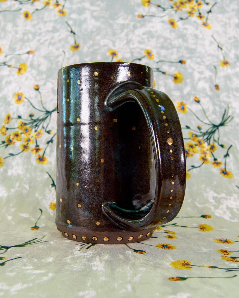 Brown ceramic mug with decorative gold dots on a floral-patterned fabric background