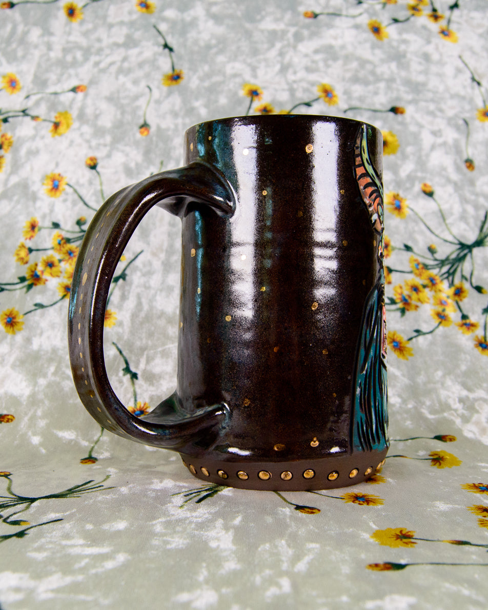 Dark brown ceramic mug with decorative gold elements on a floral-patterned background