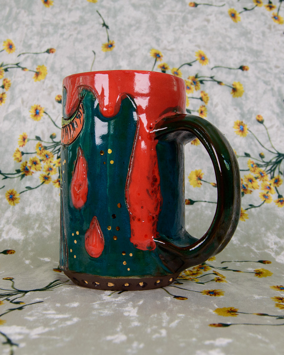 Colorful ceramic mug with red and green blood drips design on a floral-patterned background