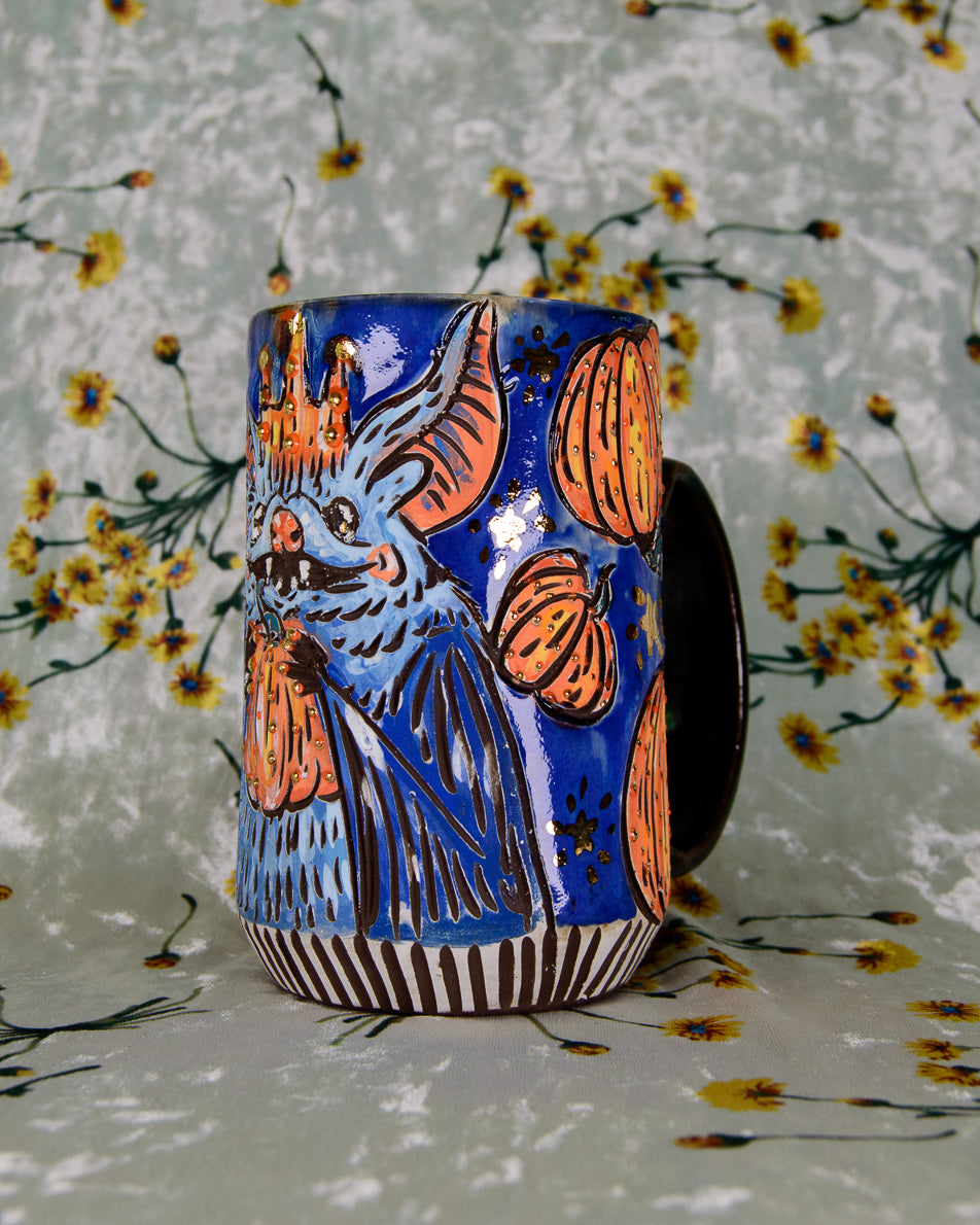 Ceramic mug with blue and orange bat with pumpkins design on a floral background