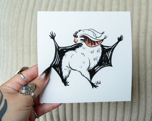 Hand holding a piece of paper with a black and white illustration of a dancing bat