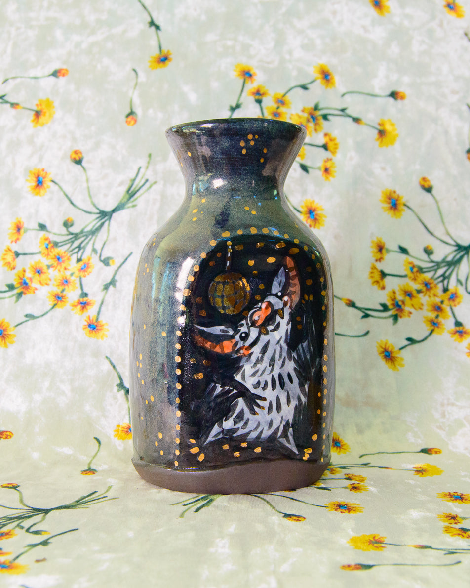 Decorative vase with a painted design of a dancing bat and gold disco ball on a floral background