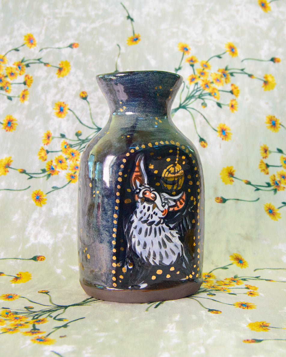 Decorative vase with a painted design of a bat on a floral background
