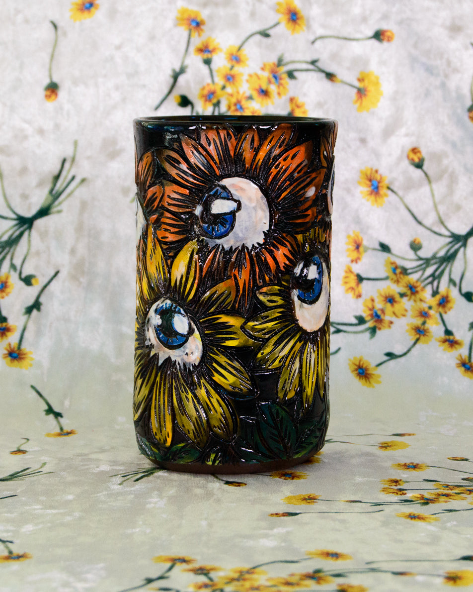 Handmade Ceramic cup with stylized eyeball flower designs in orange, yellow, and blue.
