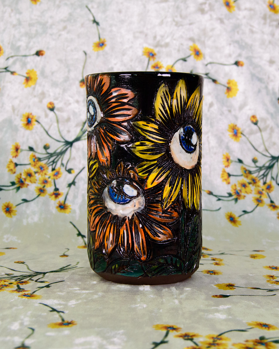 Handmade Ceramic cup with stylized eyeball floral designs in orange, yellow, and blue on a black background.