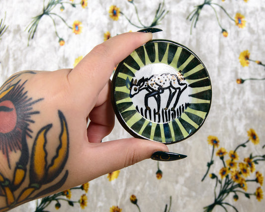 Hand holding a decorative ring dish with a black and white fawn design against a floral background