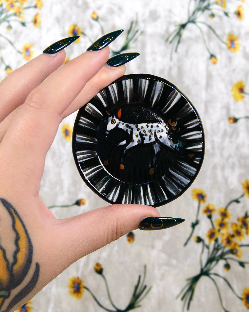 Hand holding a black and white ring dish with a fawn design on floral background
