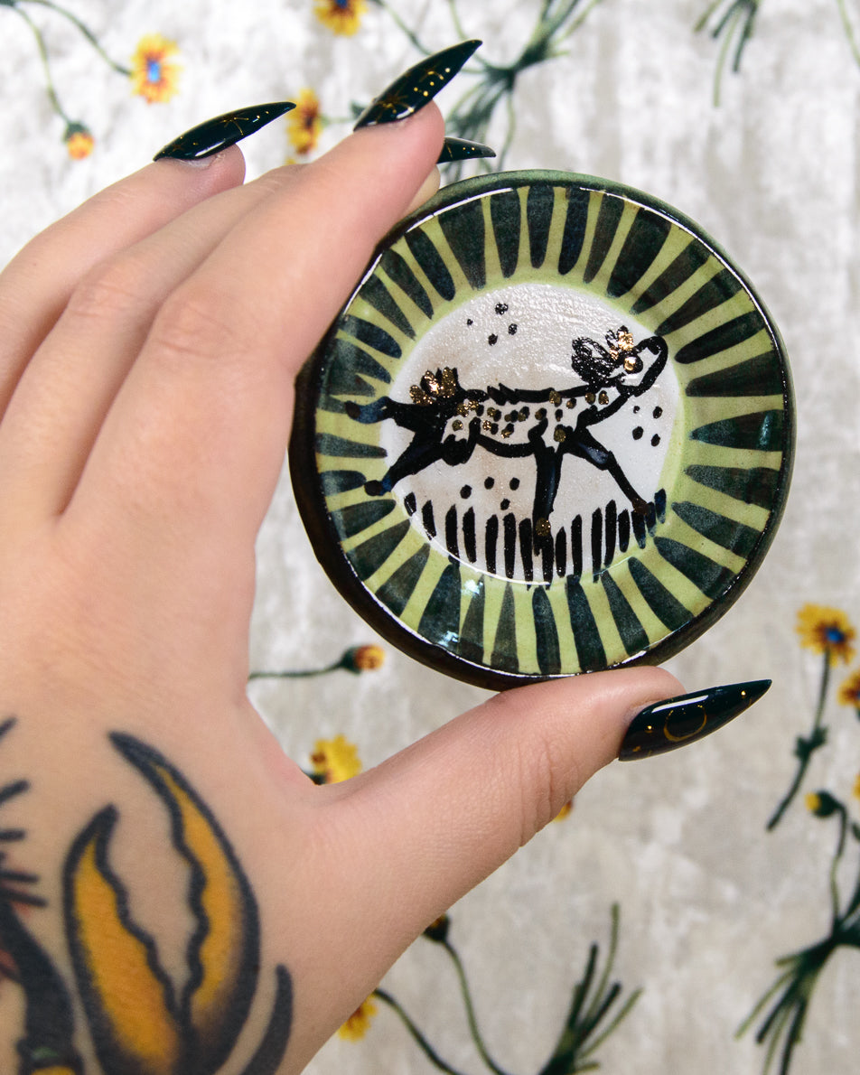 Hand holding a decorative plate with a black and white deer design against a floral background