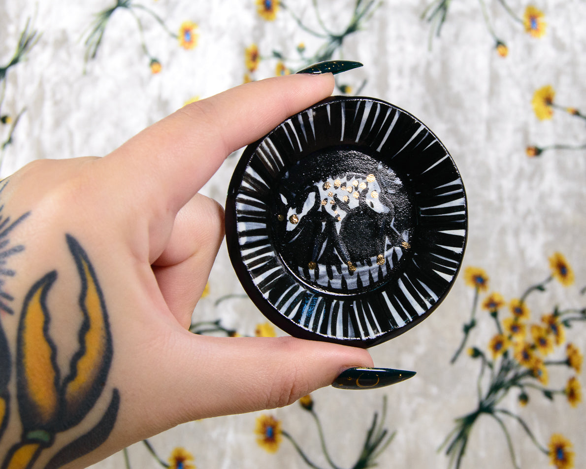 Hand holding a black ceramic dish with white deer design against a floral background