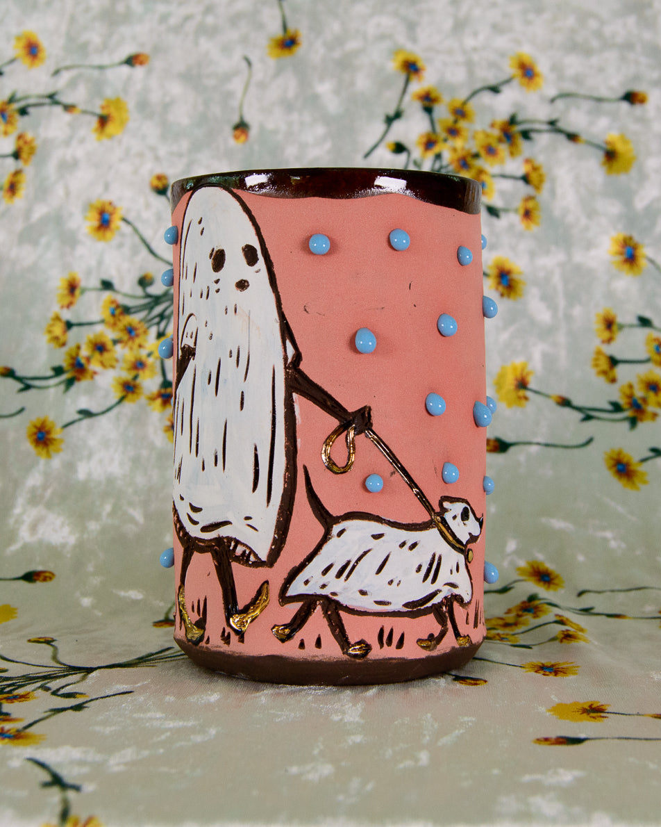 Pink mug with blue polka dots and a cartoon design of a ghost walking a dog