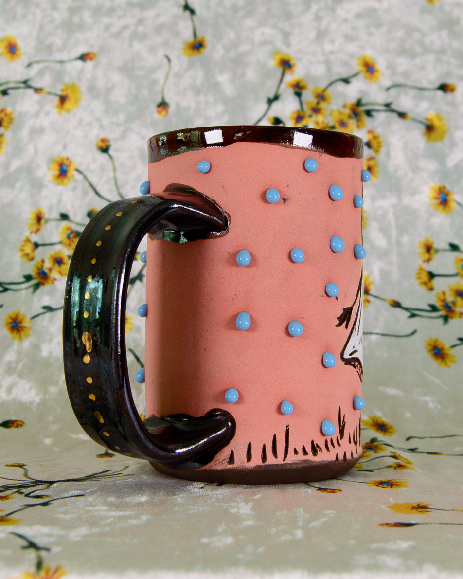 Pink mug with blue polka dots and a black handle on a floral background