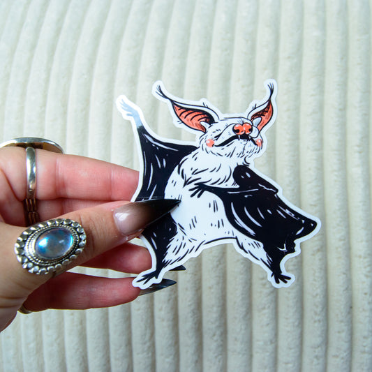 Hand holding a sticker of a bat with pink ears against a white background