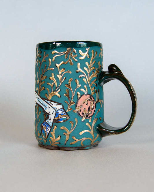 Teal mug with gold leaf design and handle on a light gray background