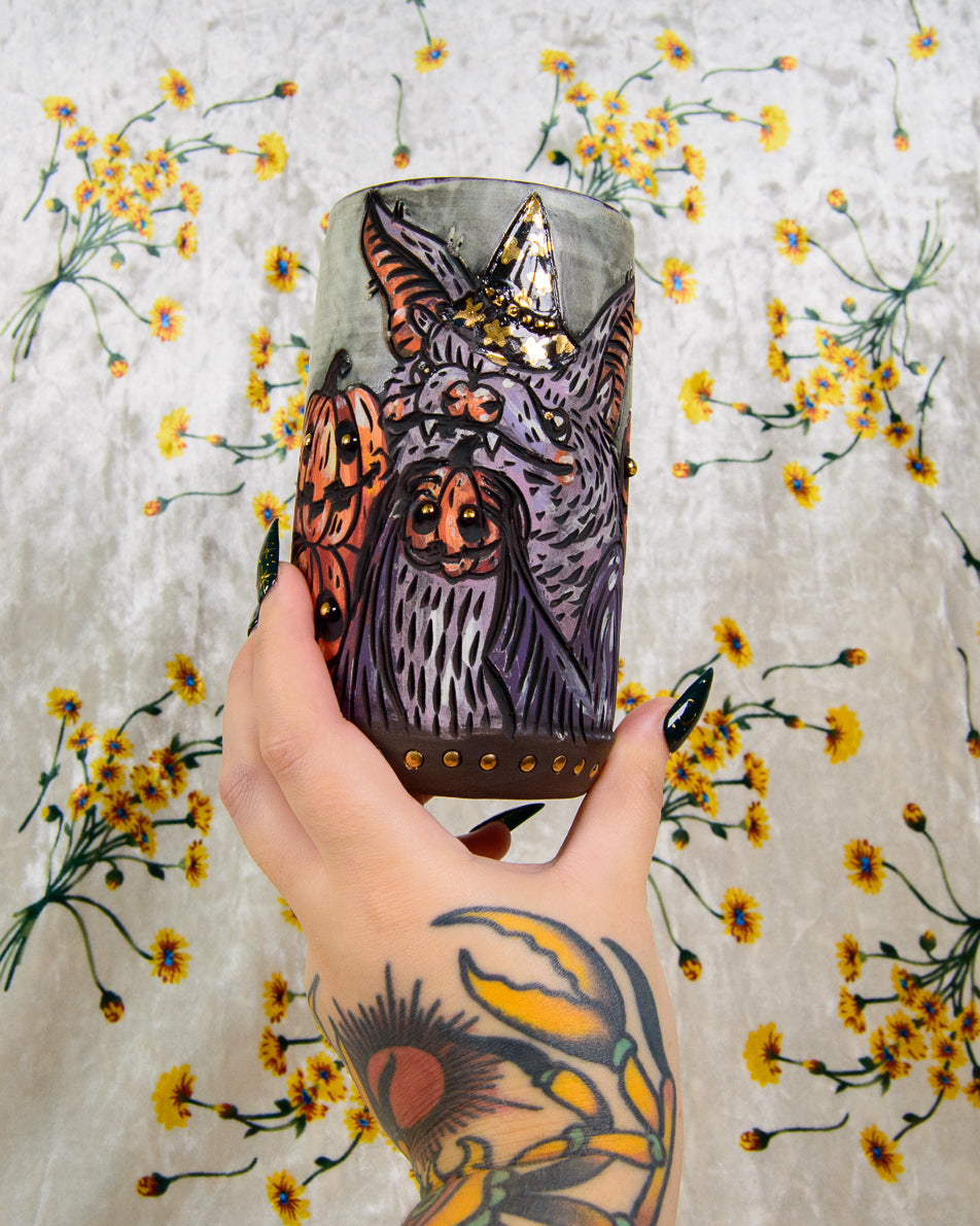 Hand holding an illustrated mug of a cartoon bat with halloween themed pumpkins