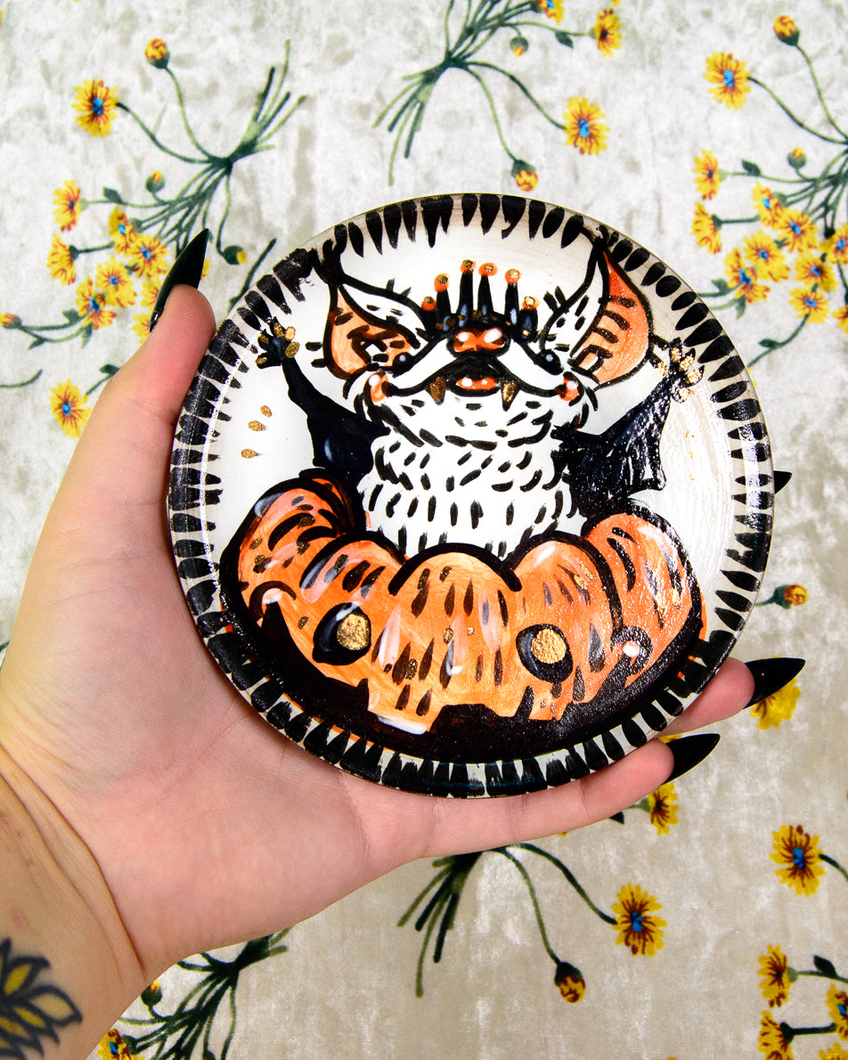 black and white ceramic coaster with a painted cartoon bat coming out of a pumpkin