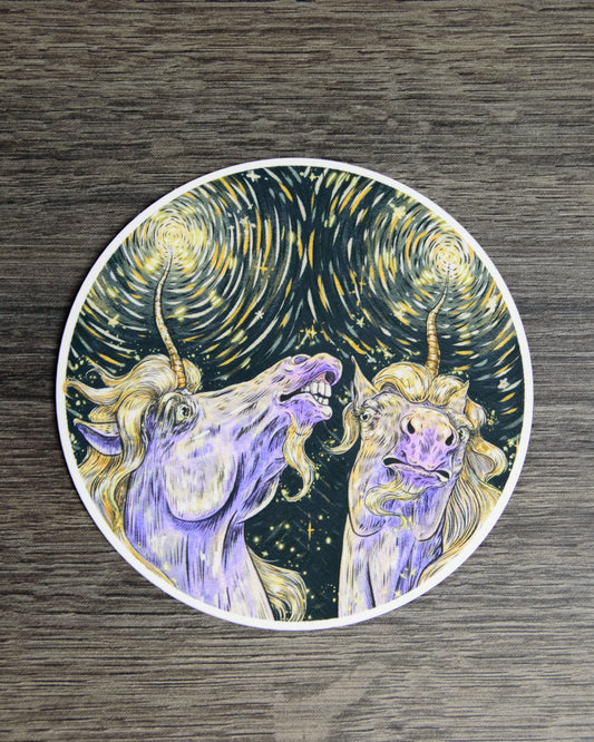 Circular sticker of two unicorns with a starry night background on a wooden surface.
