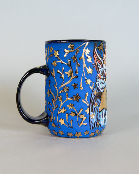 Blue mug with gold floral patterns and a bird design on a white background