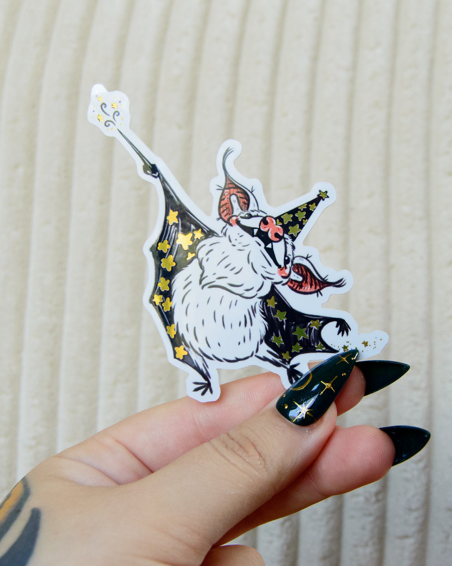 Hand holding a sticker of a wizard bat with a magic wand and gold reflective stars