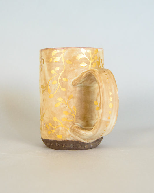 Ceramic mug with gold leaf pattern on a light gray background