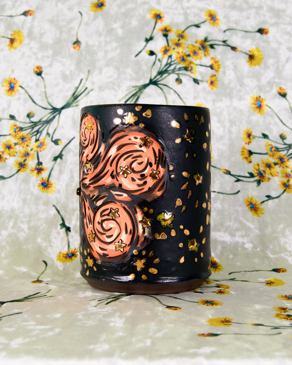 black stoneware cup with cartoon magic swirl designs and gold stars