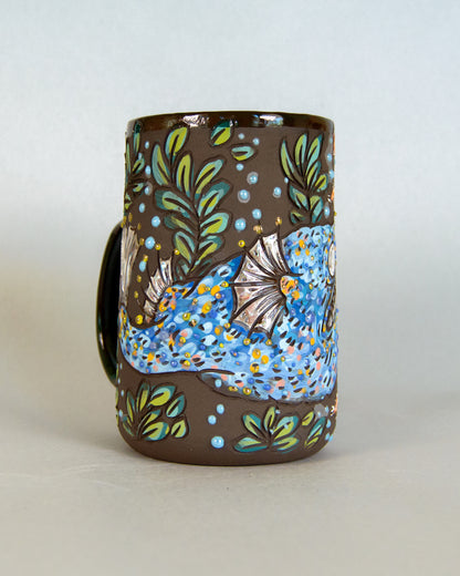 Decorative mug with fish and leaf patterns on a plain background