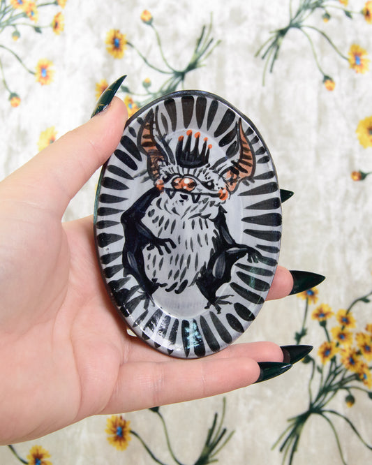 Hand holding a round black and white ring dish with a bat design on a floral background