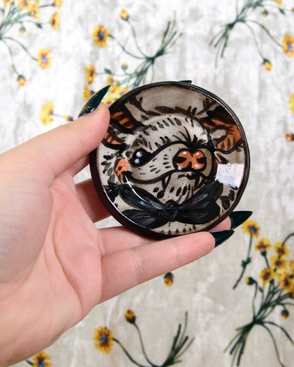 Hand holding a round ceramic coaster with a bat design against a floral background