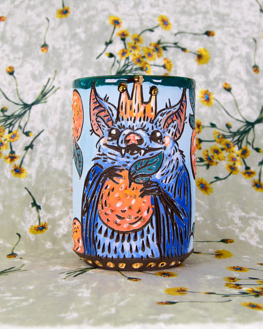 Ceramic mug with a cute illustration of a cartoon bat wearing a crown holding oranges