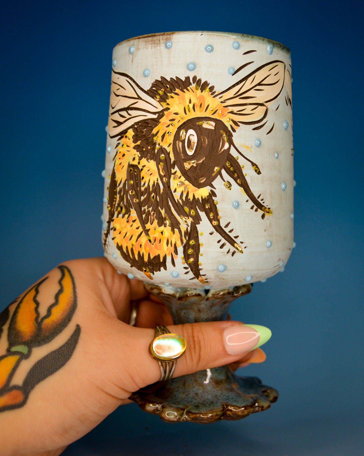 Handmade ceramic wine cup with a stylized bee design and textured blue glaze dots