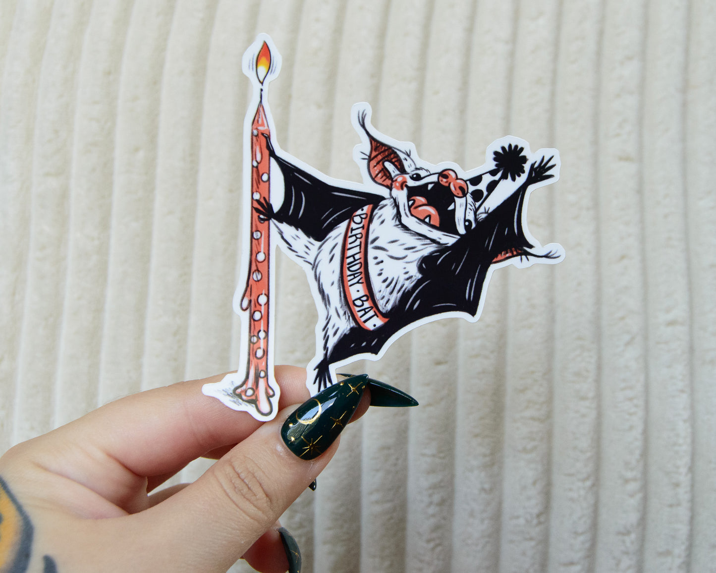 Sticker of a cute bat dancing around a birthday candle wearing a birthday sash and pointed party hat