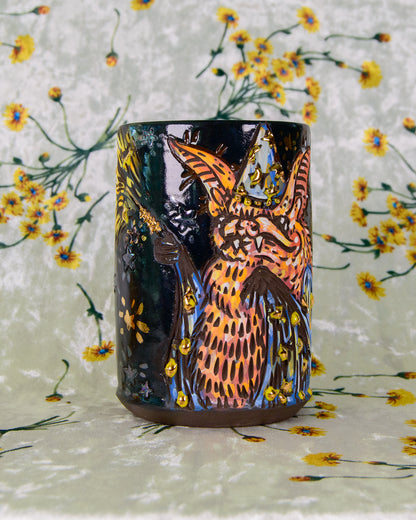 Black stoneware cup with an orange and blue cartoon wizard bat design and gold luster stars