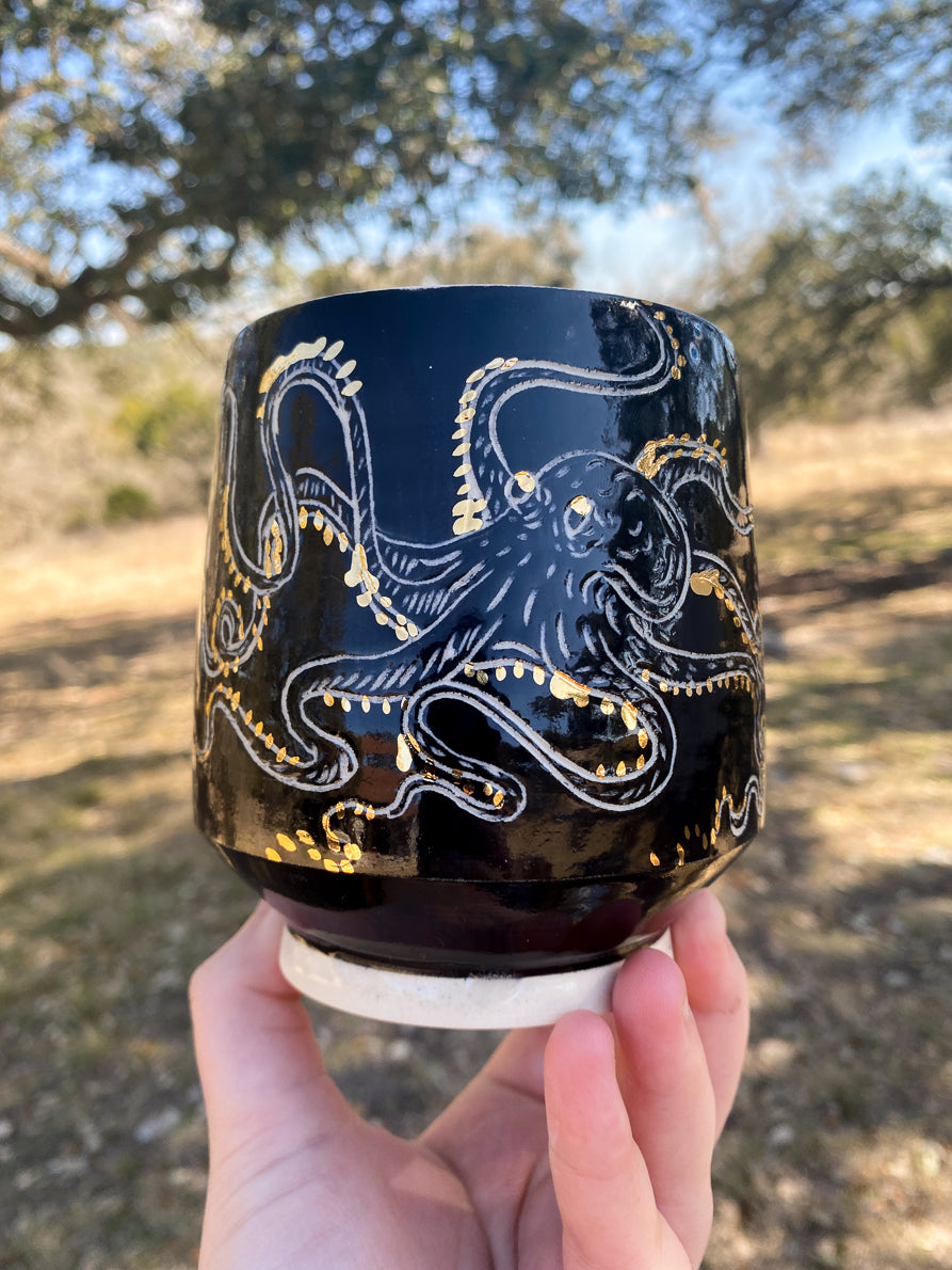 Black mug with gold and white octopus design held outdoors