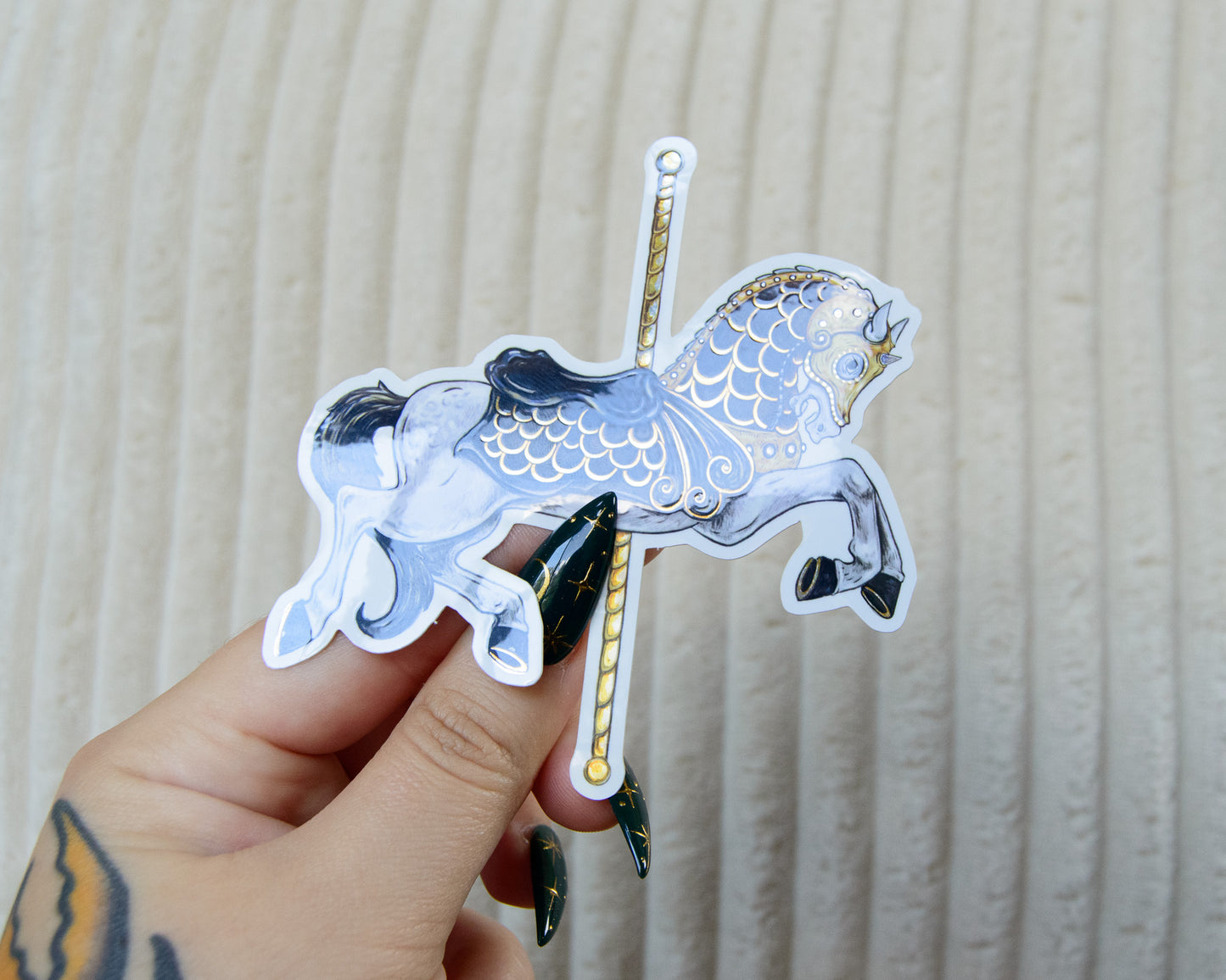 Hand holding a decorative sticker of a carousel horse with golden reflective details against a neutral background