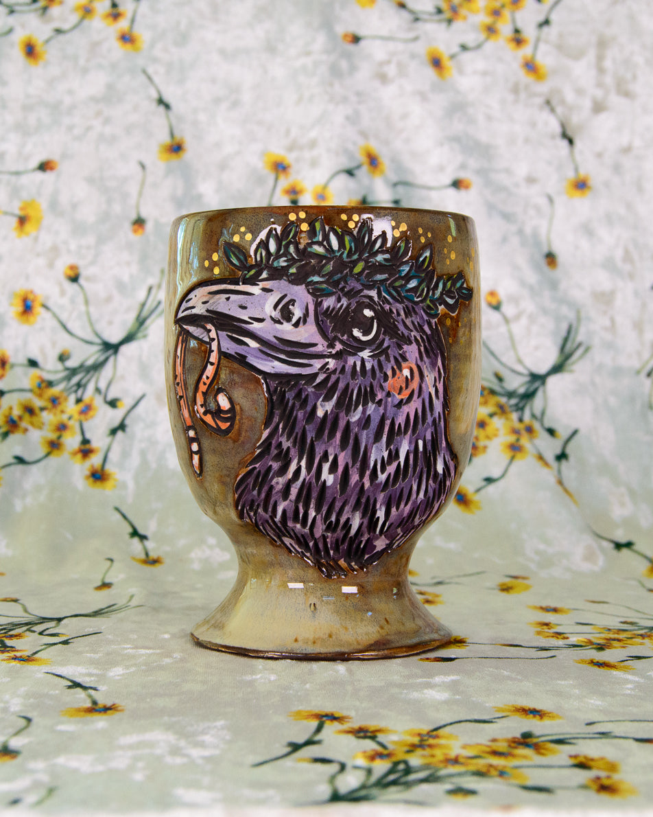 Ceramic cup with a stylized crow bird design on a floral-patterned background