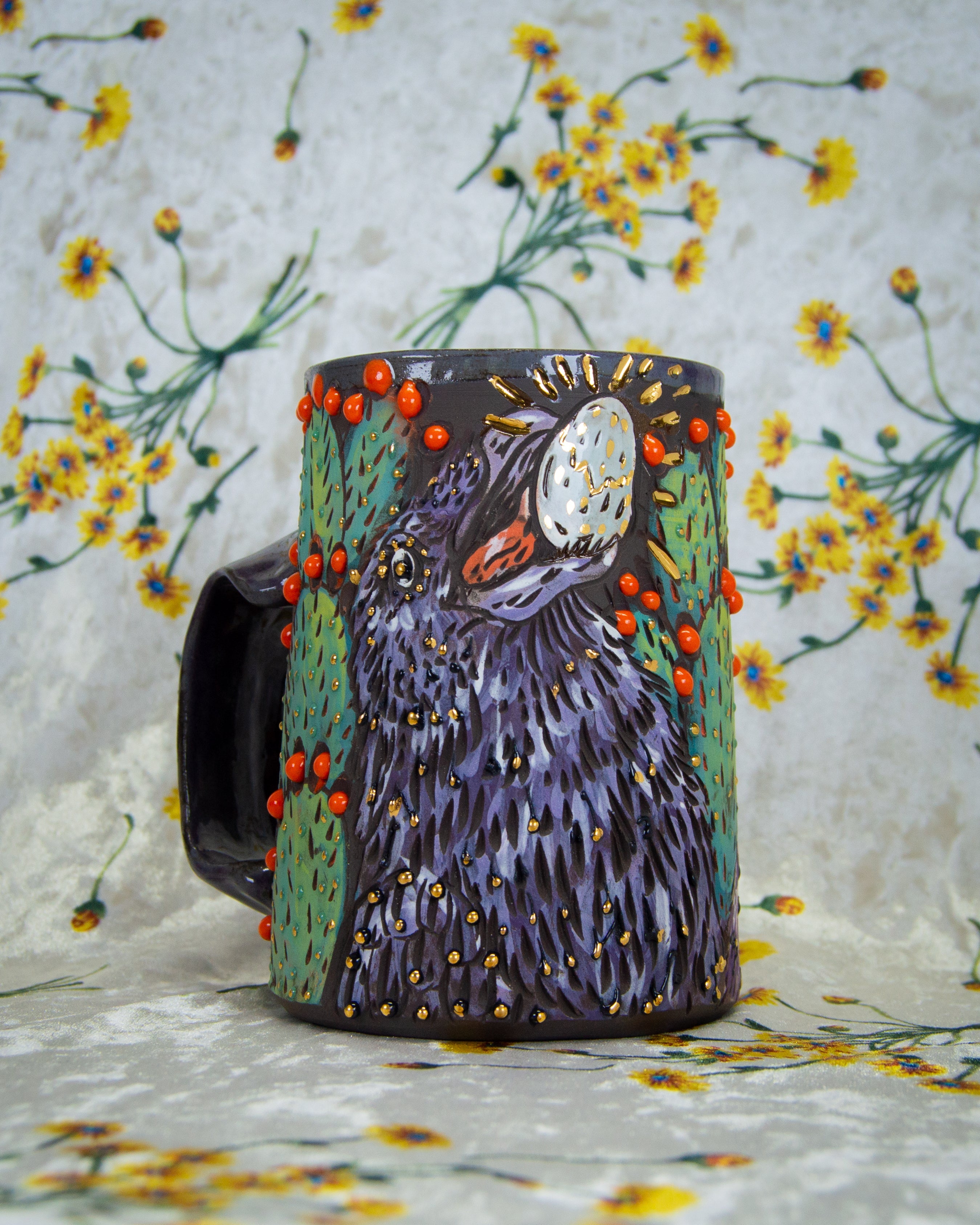Handmade ceramic mug with a crow holding an egg and colorful prickly pear cactus