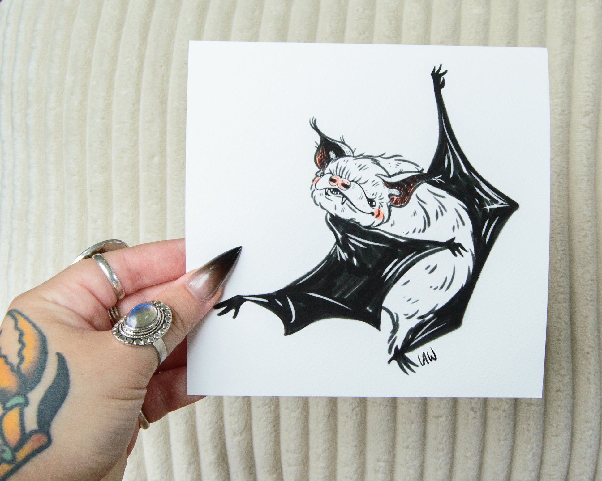 Hand holding a card with a black and white illustration of a bat on a textured beige background.