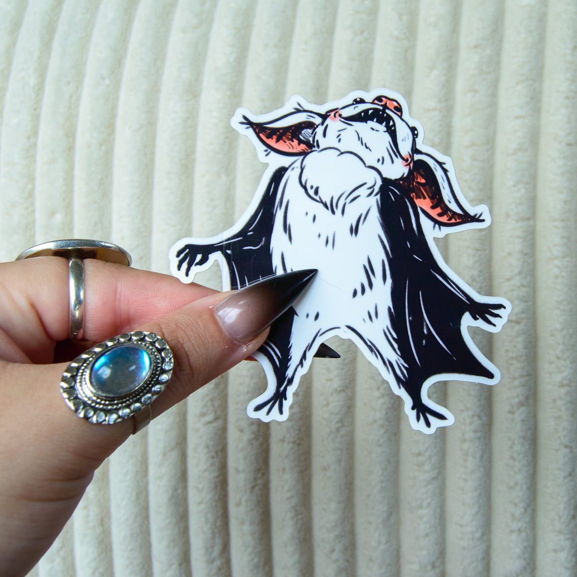 Hand holding a sticker of a bat with pink accents against a white background