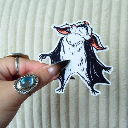 Hand holding a sticker of a bat with pink accents against a white background