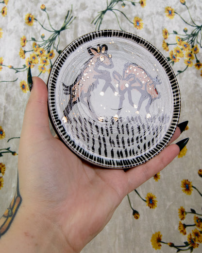 Hand holding a decorative plate with a deer design against a floral background